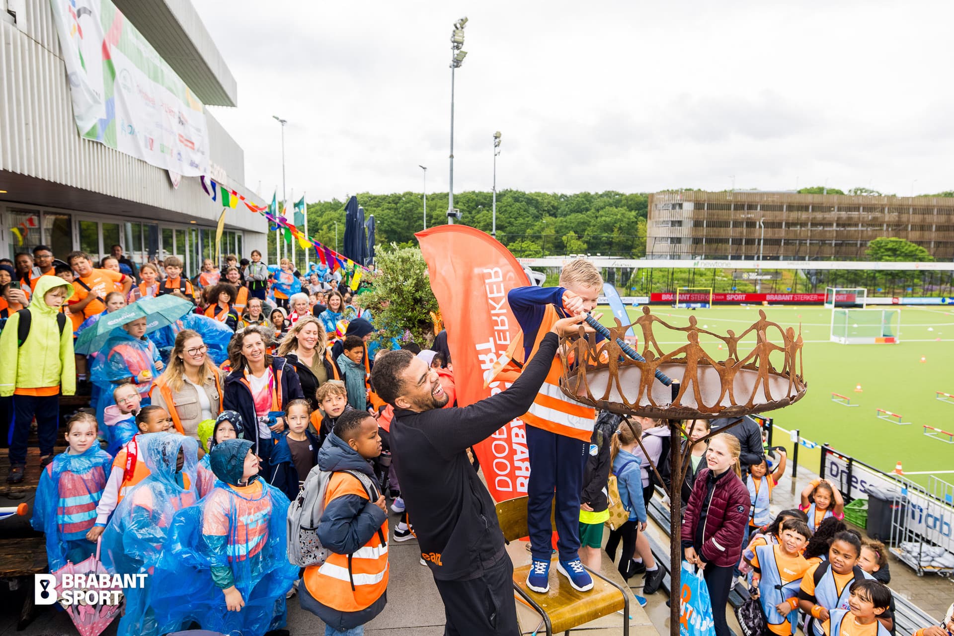Foto waar een jongetje met hulp van een volwassen man het Olympisch kinderspelen vuur aansteekt
